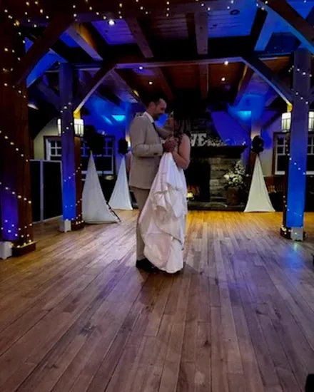 A couple sharing a first dance beneath timber beams and blue lighting.